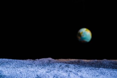 textured ground with blurred planet Earth in space isolated on black clipart