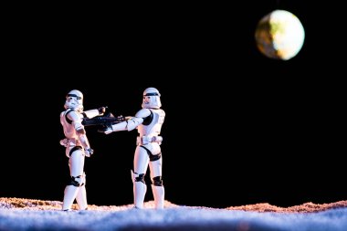 imperial stormtrooper aiming with weapon at another on black background with planet Earth