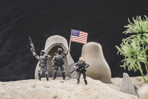 selective focus of toy soldiers with guns and american flag standing near caves on sand dune 