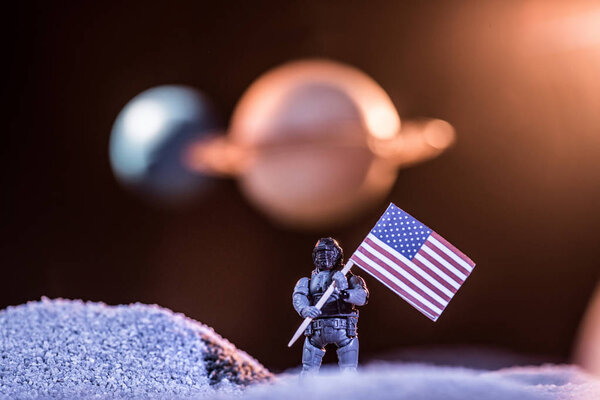 selective focus of toy astronaut holding american flag in space 