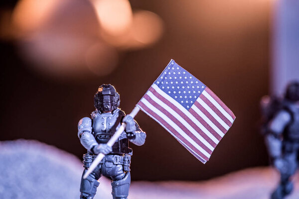 selective focus of toy astronaut holding national american flag in space 
