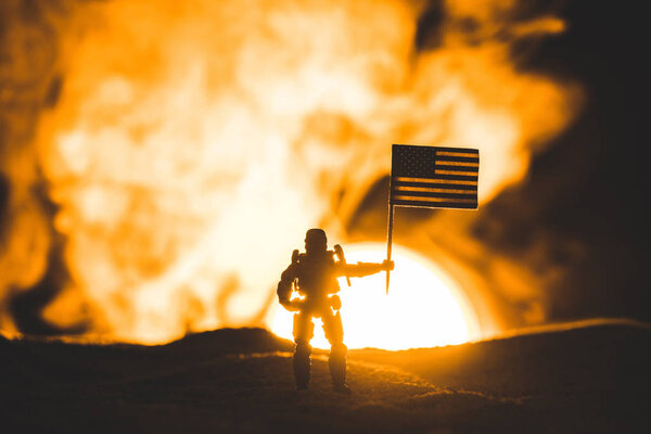 Силуэт солдата-игрушки с американским флагом на планете с солнцем в дыму
 