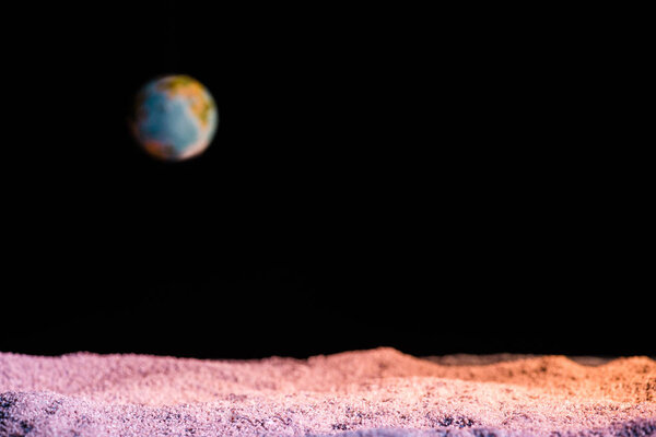 selective focus of textured ground with blurred planet Earth in space isolated on black