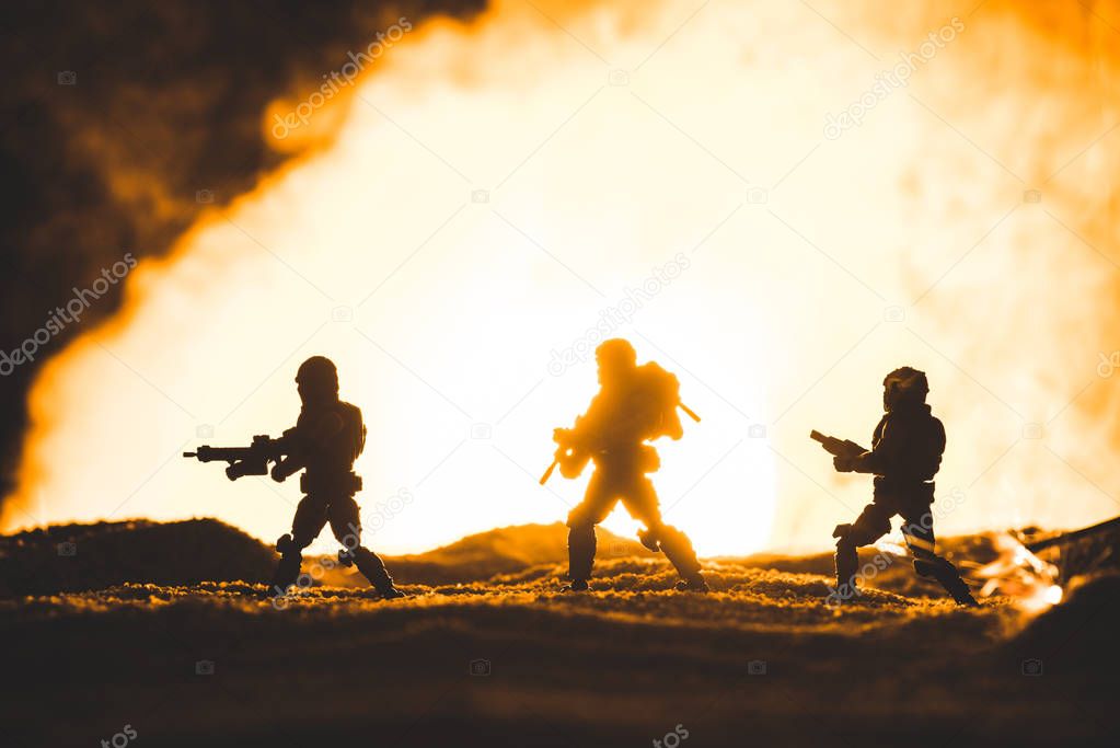 silhouettes of toy soldiers with guns walking on planet with sun in smoke on background