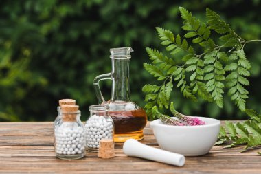 selective focus of pestle near mortar with flowers, glass bottles with pills and jug with oil on wooden table  clipart