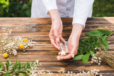 cropped view of woman holding glass bottles with pills near plants  clipart