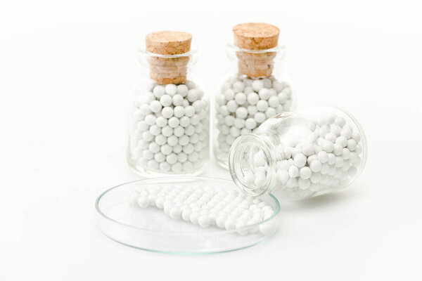 selective focus of round pills in glass petri dish near bottles with wooden corks isolated on white 