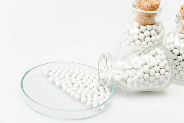 selective focus of small pills in glass petri dish near bottles with wooden corks isolated on white 