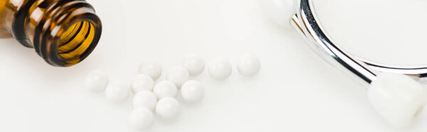 panoramic shot of round small pills near stethoscope and glass bottle on white 