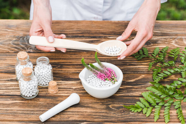 top view of woman holding spoon with pills near mortar with veronica flowers and green leaves on wooden table 