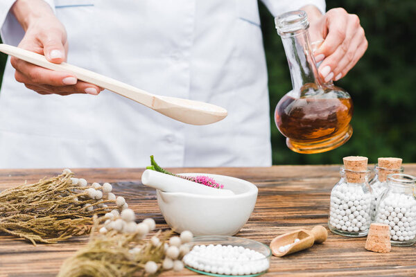 selective focus of woman holding spoon and jug with oil near mortar with veronica flowers on wooden table 