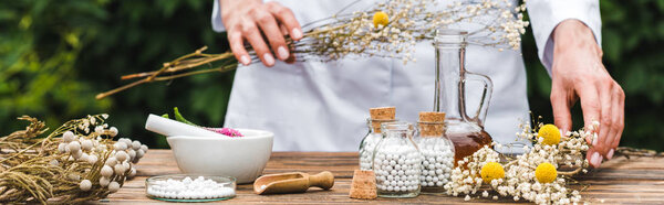 panoramic shot of woman holding gypsophila flowers near bottles with pills 
