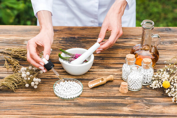 обрезанный вид женщины, держащей пипетку рядом с маленькими круглыми таблетками на деревянном столе
 