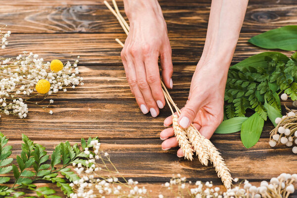 cropped view of woman holding wheat near plants on wooden table 