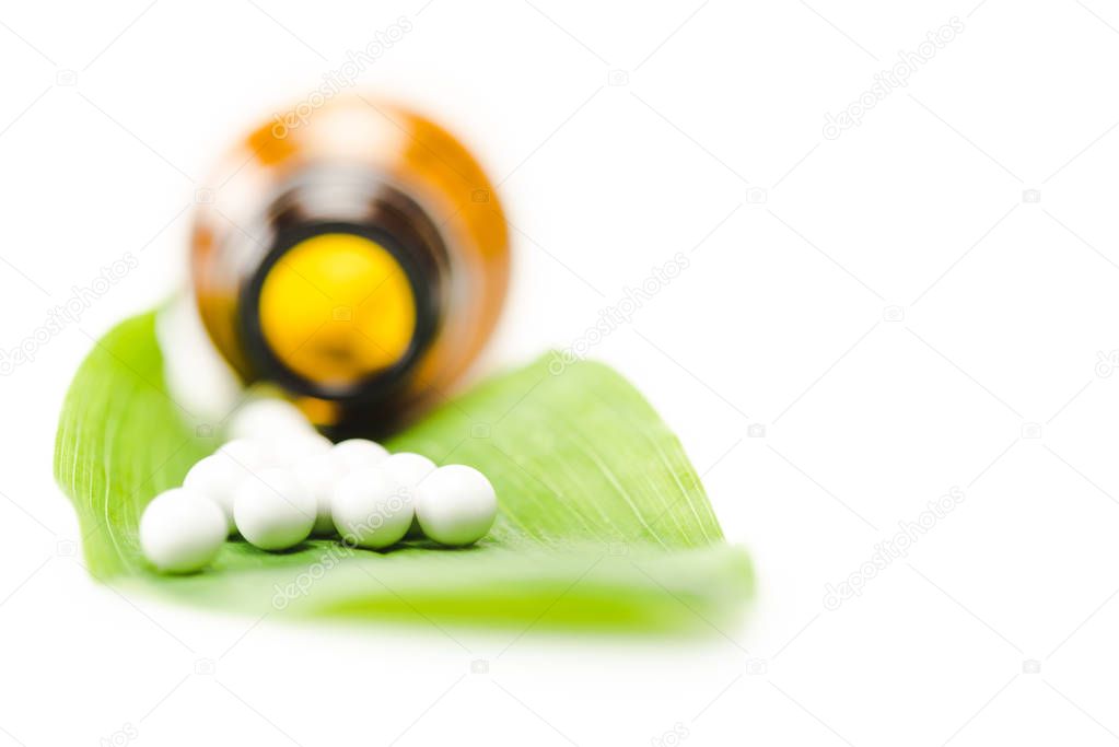 selective focus of small round pills on green leaf near bottle isolated on white 