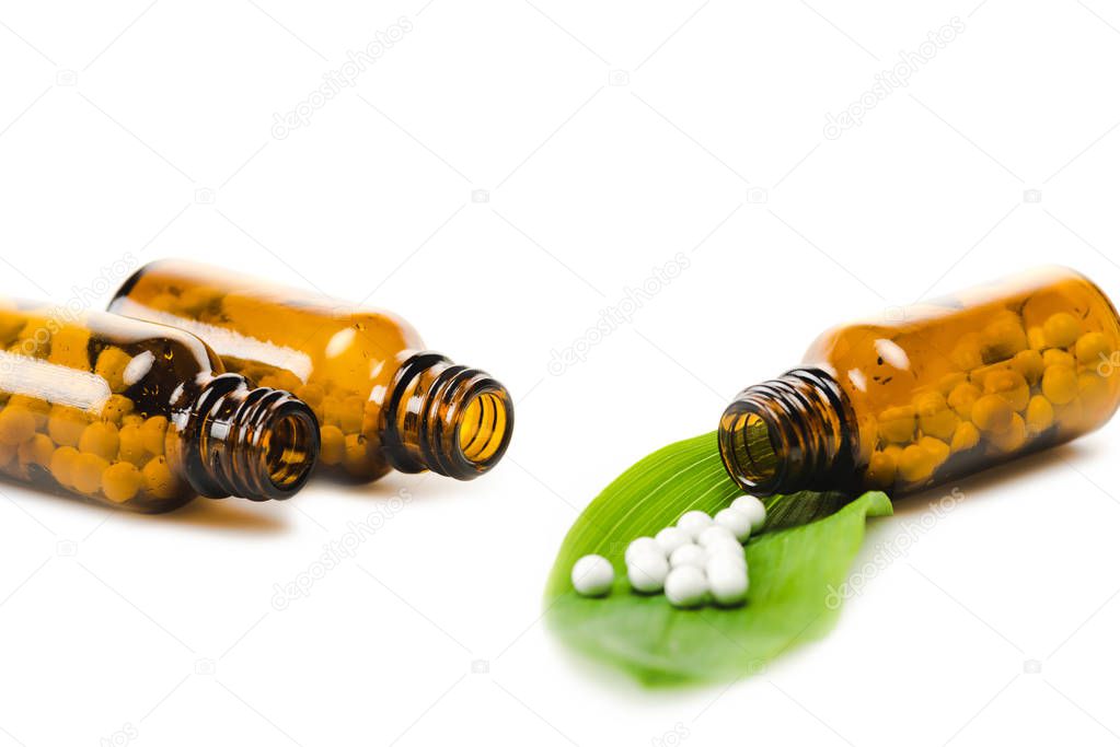 selective focus of bottles with medicine near green fresh leaf isolated on white 
