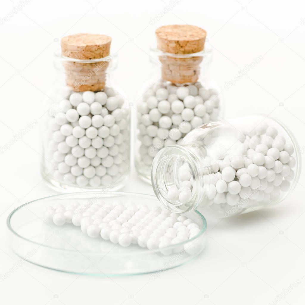 Selective focus of bottle with round small pills near glass petri dish isolated on white