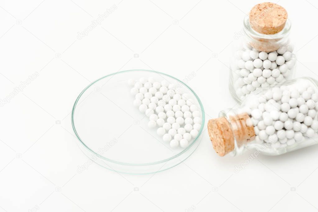 selective focus of round small pills in glass petri dish near bottles with wooden corks isolated on white 