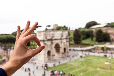 ROME, ITALY - JUNE 28, 2019: partial view of man showing okay sign in front of arch of constantine clipart