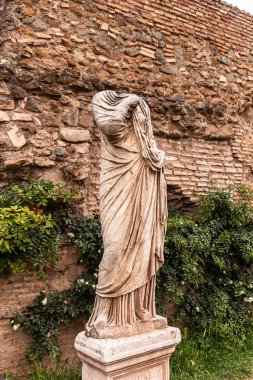 ROME, ITALY - JUNE 28, 2019: ancient headless statue near brick wall and green plants clipart