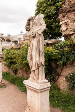 ROME, ITALY - JUNE 28, 2019: ancient headless statue near old wall and green plants clipart