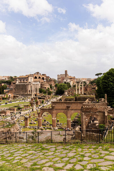 ROME, ITALY - JUNE 28, 2019: tourists near ancient buildings at roman forum under blue sky