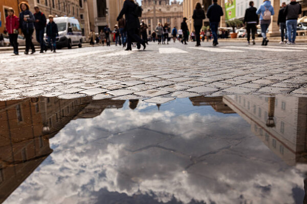 ROME, ITALY - JUNE 28, 2019: selective focus of people walking around street and puddle on foreground in rome, italy