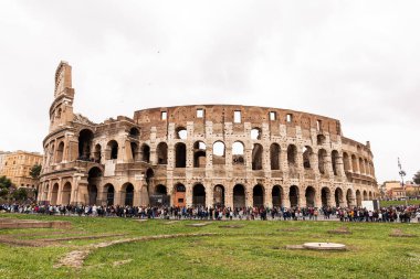 ROME, ITALY - JUNE 28, 2019: colosseum and crowd of tourists under grey sky clipart