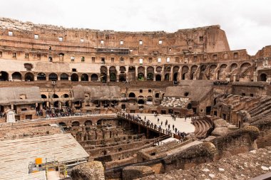 ROME, ITALY - JUNE 28, 2019: ruins of colosseum and crowd of tourists under grey sky clipart