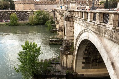 Roma, İtalya - 28 Haziran 2019: Tiber Nehri ve bulutlu gökyüzünün altındaki eski köprüdeki insanlar