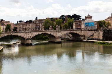 ROME, ITALY - JUNE 28, 2019: river Tiber and people on old bridge under cloudy sky clipart