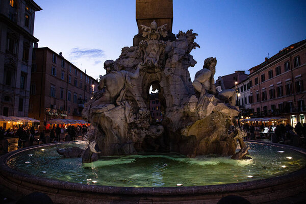 ROME, ITALY - JUNE 28, 2019: crowd of people near fountain with sculptures in evening