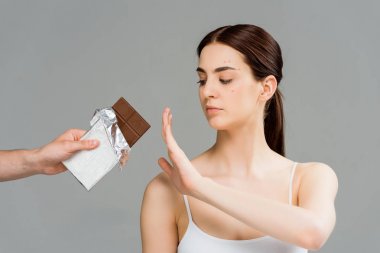cropped view of man holding chocolate bar near brunette woman with acne isolated on grey 