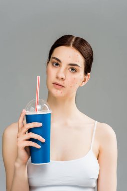 gri izole plastik bardak tutan yüzünde akne ile üzgün genç kadın 