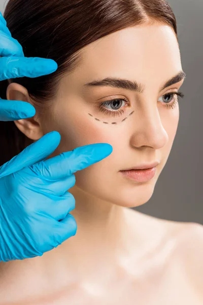在乳胶手套附近的妇女与灰色隔离在脸上的痕迹的整形外科医生的裁剪视图 — 图库照片