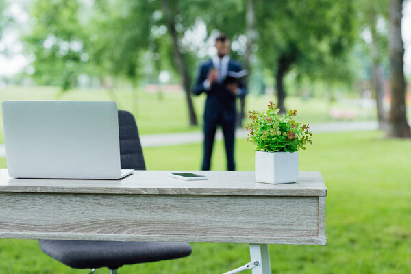 selective focus of table with flowerpot and laptop in park 
