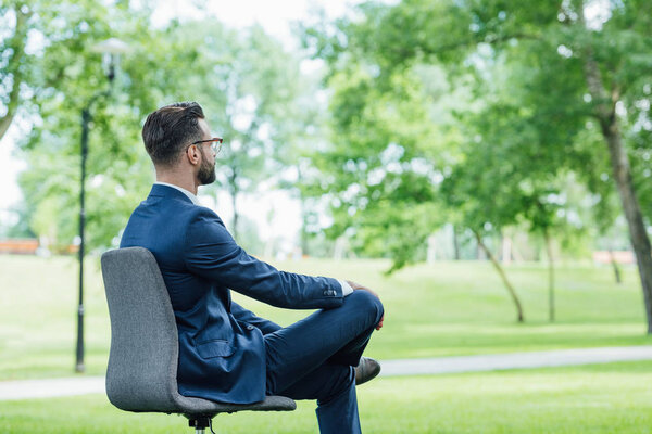 young businessman sitting in office chair in park and looking forward