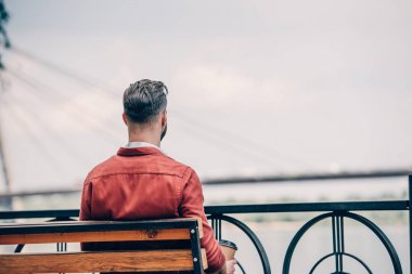 kırmızı gömlekli adamın arka görünümü bankta oturan ve gitmek için kahve tutarak 