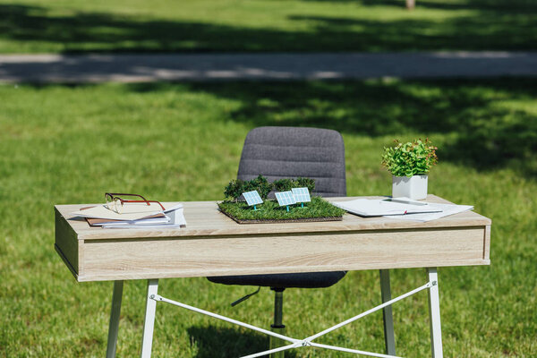 table with sun batteries layout, flowepot, notebooks and glasses near office chair in park