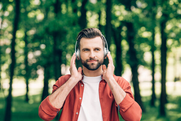 young man standing in park, listening to music and looking away