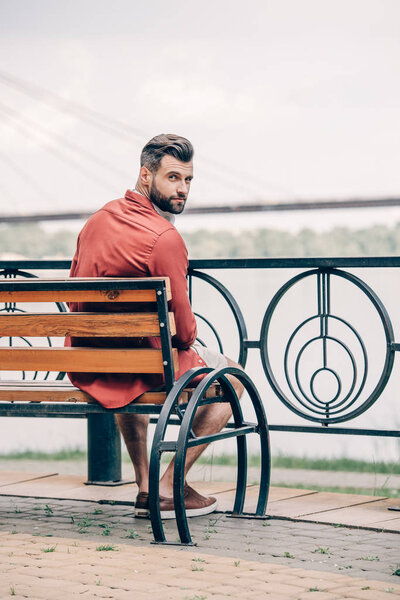 handsome man sitting on bench and looking at camera
