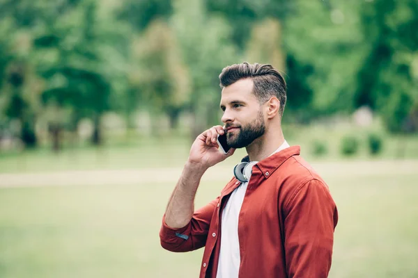 Junger Mann Steht Park Und Spricht Mit Smartphone — Stockfoto