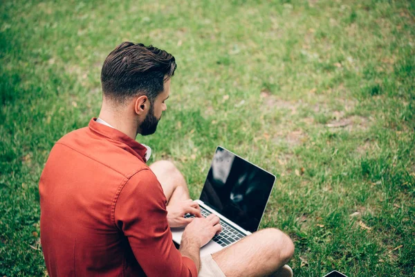 坐在草地上的人的后视图 并使用笔记本电脑 — 图库照片