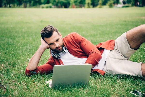 年轻人躺在草地上 在公园里 使用笔记本电脑 — 图库照片