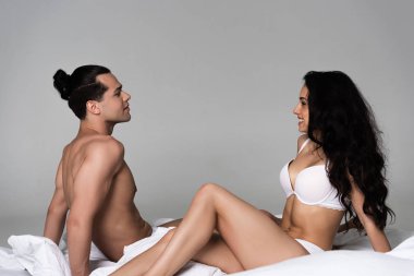 smiling sexy couple in underwear sitting on bed face to face clipart