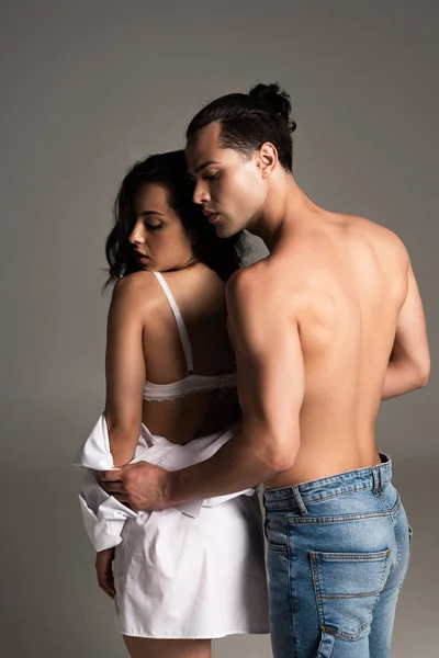 shirtless muscular man with sexy girlfriend in white underwear with closed eyes on grey