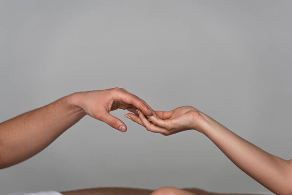partial view of young couple touching hands isolated on grey