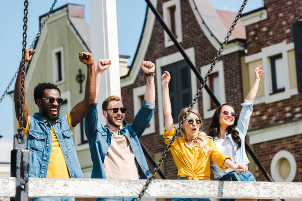 cheerful group of multicultural friends in sunglasses celebrating triumph 