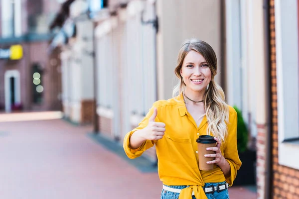 通りに立ち 親指を上げながら紙コップを持つ幸せな女性 — ストック写真