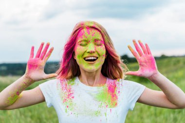 kapalı gözleri ve elleri gesturing ve açık havada gülümseyen pembe holi boya ile neşeli kadın 